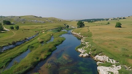 A tranquil river winding through a vibrant green valley beneath a bright, clear blue sky