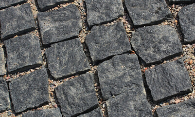An angled view of evenly laid rows of dark granite paving stones
