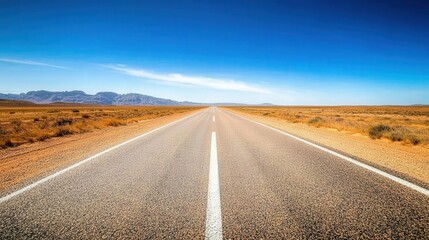 Fototapeta premium Long desert road stretching to horizon, barren landscape with mountain background, bright sunlight, sense of solitude,
