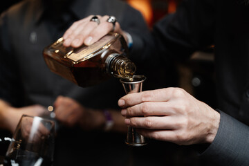 Bartender pouring liquor into a jigger in a lively bar setting at night