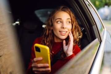 Young woman with a smartphone in her hands in the back seat of a car.  Traveling by car....