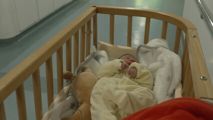 Close-up shot of a baby in a wooden crib being gently pushed through a hospital corridor,...
