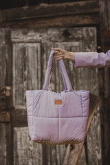 Hand holding a pink shopping bag against the background of an old wooden door