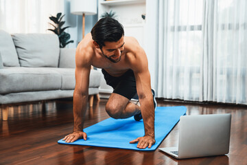 Athletic and sporty man doing mountain climber on fitness mat during online body workout exercise...