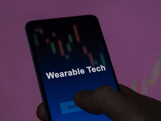 An investor analyzing the wearable tech etf fund on a screen. A phone shows the prices of Wearable Tech