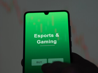 An investor analyzing the esports & gaming etf fund on a screen. A phone shows the prices of Esports & Gaming
