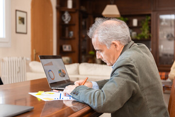 Senior man analyzing data and graphs on a laptop at home