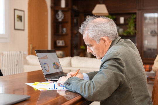 Senior man analyzing data and graphs on a laptop at home