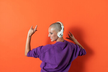 Bald adult woman in purple sweater enjoying music on headphones