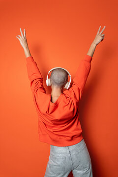 Back view of person in orange enjoying music in headphones and dancing