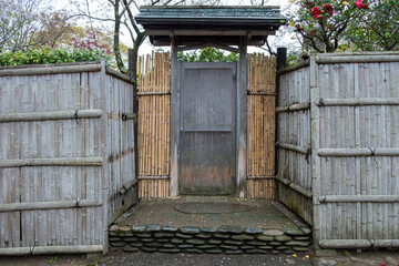 Traditional Japanese garden gate, a wooden door with a small roof framed by bamboo fences