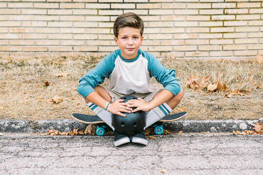 Boy with skateboard and helmet sitting on pavement