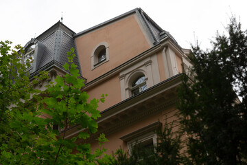 As you gaze upwards at a tall building, lush trees stand in front of it, creating a beautiful natural frame for the architectural structure