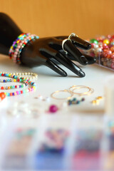 Hand figurine, colorful friendship bracelets, necklaces, various beads and DIY supplies on the table. Making jewelry at home. Selective focus.