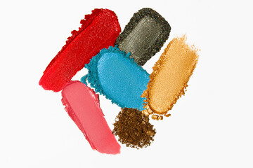 Cosmetic product texture composition with lipstick, eyeshadow, bronzer, glitter, and powder on a light white background.