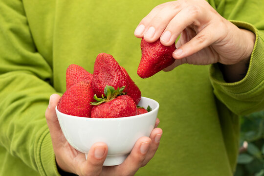 ordenado frutillas para el postre. Mano tomando una frutilla para dejarla en un tiesto de cer&aacute;mica blanca, fondo verde claro
