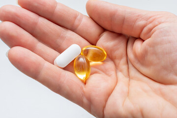 Close up of female open palm with yellow Omega-3 fatty acid capsules and magnesium tablets on light background. Concept of taking additional vitamins and minerals during menopause in women.