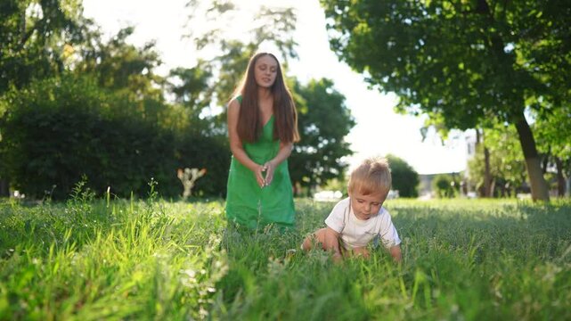 The baby takes his first steps on the grass. Child mother family concept. A mom teaches her baby to walk. Mom teaches her baby to walk on the grass and then steps down lifestyle.