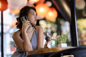 Woman enjoying ice cream while talking on smartphone in a decorated cafe with warm lighting and vibrant ambiance