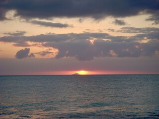 Golden hues of a sunset reflecting off the water, with driftwood scattered along the shoreline.
