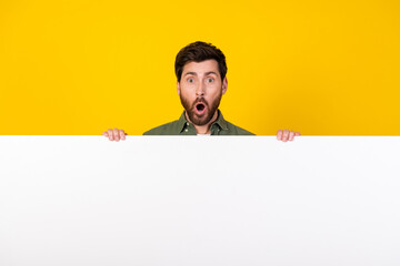 Photo of nice young man behind empty space ad wear shirt isolated on yellow color background