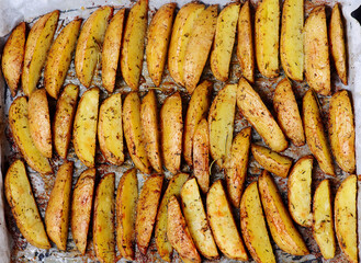 Roasted  potato wedges with olive oil and herbs on a baking sheet.style rustic.selective focus