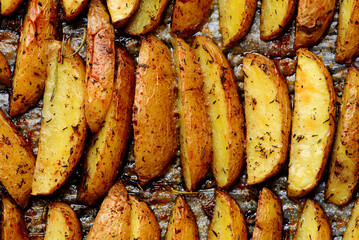 Roasted  potato wedges with olive oil and herbs on a baking sheet.style rustic.selective focus