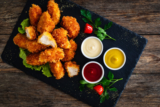 Fried breaded chicken nuggets served with mayonnaise, ketchup and mustard on wooden table	 - Powered by Adobe