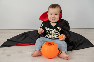 Cute caucasian boy in dracula halloween costume holding candy basket on white background. 