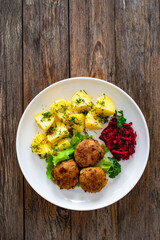 Fried meatballs, boiled potatoes, beetroots and fresh vegetables served on white plate on wooden table