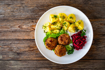 Fried meatballs, boiled potatoes, beetroots and fresh vegetables served on white plate on wooden...