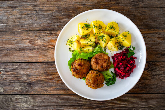 Fried meatballs, boiled potatoes, beetroots and fresh vegetables served on white plate on wooden table