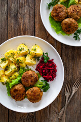 Fried meatballs, boiled potatoes, beetroots and fresh vegetables served on white plate on wooden table