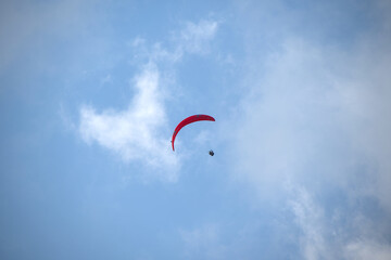 Paraglider with a vibrant red canopy gliding through the sky surrounded by soft white clouds.