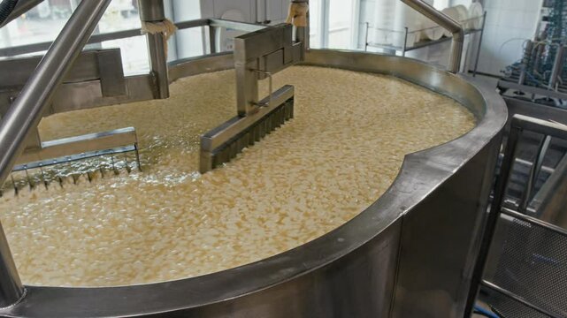No people medium closeup of large curd cutters spinning around in automated coagulation vat at cheese factory, cutting yellow dairy mixture into pieces
