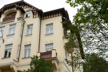 A sizable white building featuring a balcony and accompanied by beautiful trees located right in front of it, enhancing the view