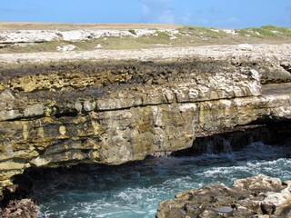 Rugged limestone cliffs with ocean waves crashing below, showcasing raw coastal beauty.