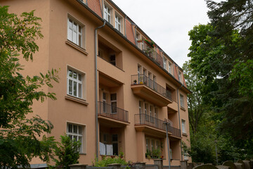 A substantial apartment building featuring multiple balconies, with lush trees situated in front of it, creating a serene ambiance