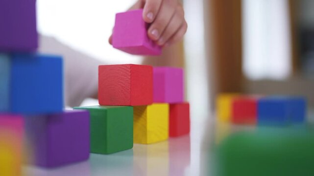 Girl daughter plays with blocks, builds. Play toddler kid concept. The child plays with blocks and lifestyle cubes, fine motor. skills. A girl plays with cubes and blocks in a building in kindergarten