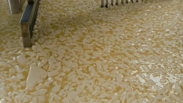 No people closeup of wire frames rotating in automated heating vat at cheese plant, cutting yellow mass into pieces and separating it from whey
