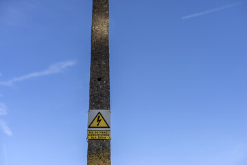 Betonowy słup podtrzymujący przewody napowietrznej linii elektroenergetycznej z charakterystyczną tabliczką ostrzegającą o niebezpieczeństwie porażenia prądem © qrrr