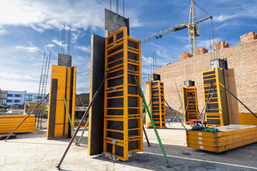 Construction site with yellow column formwork and brick wall, ready for concrete pouring