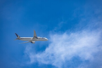 A serene image of an airplane cruising through a vivid blue sky, accompanied by soft, wispy clouds....