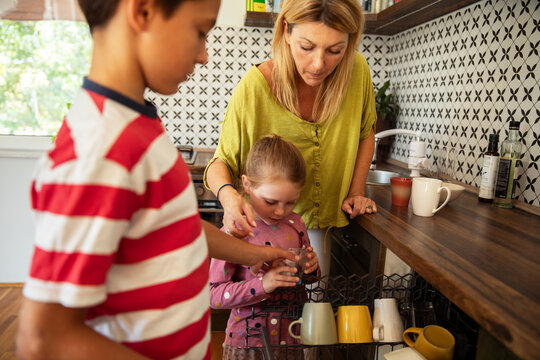 Mother teaching kids to load the dishwasher as part of family chores