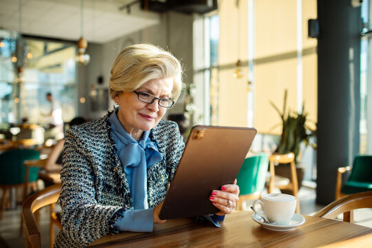 Elegant senior woman using tablet in a cozy cafe with coffee