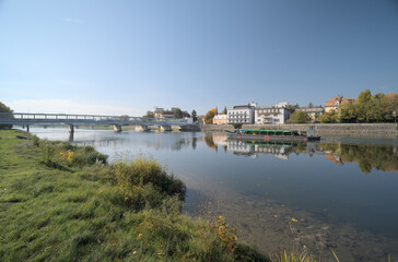 Obraz premium Riverside town with buildings and trees reflecting in calm water.