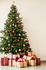 Beautiful decorated Christmas tree with a pile of presents on a simple minimalistic light colored wall background. Background with copy space for postcard or banner