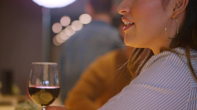 Woman holds a glass of red wine as she chats with the bartender at a modern luxury bar
