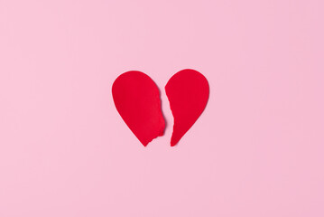 Red paper heart torn into two halves on pastel pink background. Broken heart concept, top view