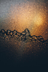 Close-up of frosty patterns on glass with warm golden light creating a glowing winter texture. Abstract natural winter theme.
